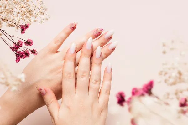 Spring manicure of woman hands with white gel polish and dried flower design.